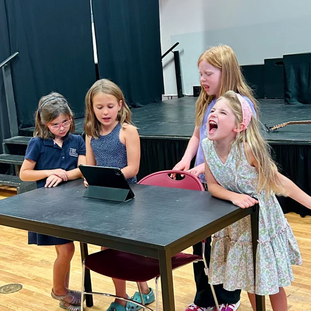 Program - Group Singing Classes A small group of students gathering around a tablet to learn a new song during a group singing class in Mount Pleasant.