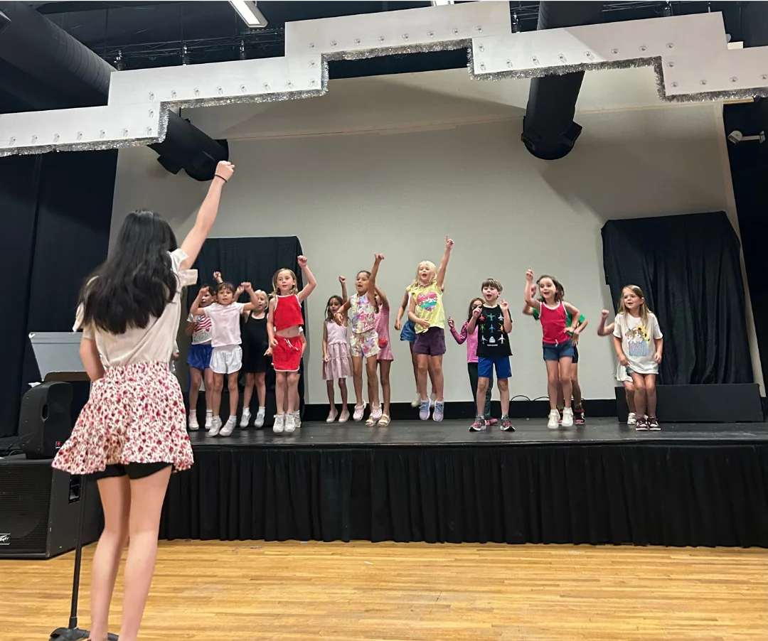 Student Spotlight - WonderStage Joy A smiling young girl holding soft pink poms during preschool music lessons at FAME Performing Arts in Mount Pleasant.