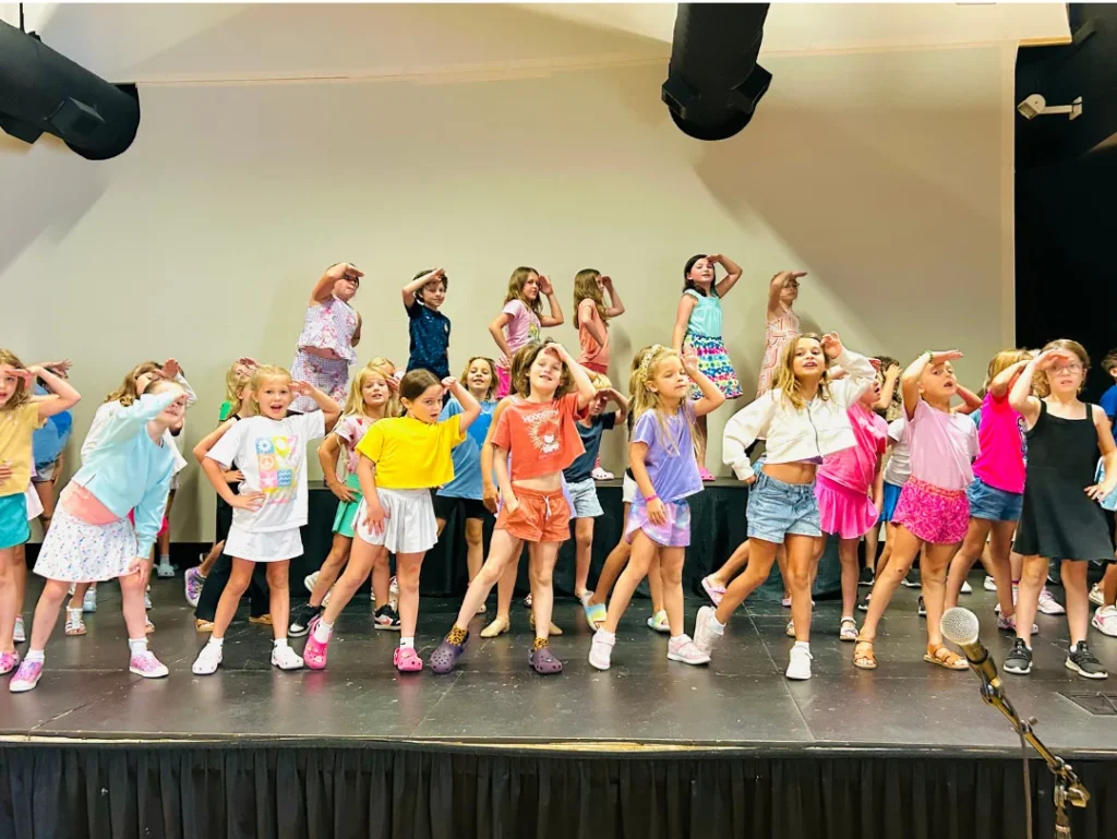 Children striking a dramatic unified pose on stage during a FAME summer theatre camp performance.