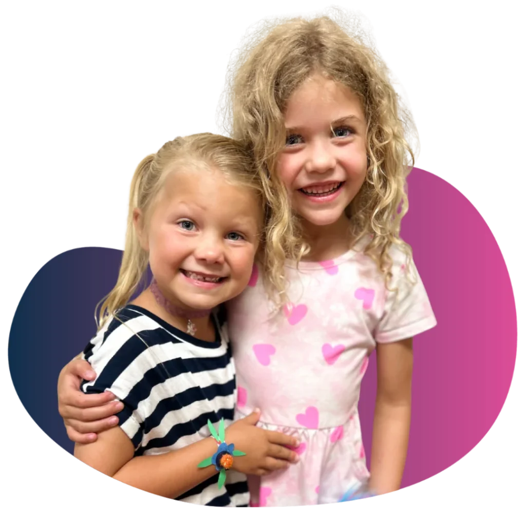 Two young girls smiling and hugging arm-in-arm in a FAME Kids Troupe performing arts class.