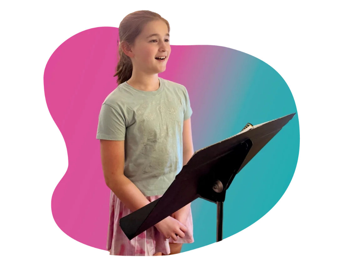 Group Voice Lessons - Singing Student - FAME Performing Arts Young girl smiling while looking at sheet music on a stand during kids group voice lessons.